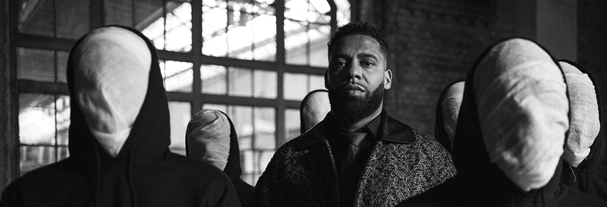 Es ist der Rapper Kurdo zu sehen, der auf einer Dachterasse steht, während im Hintergrund die Sonne untergeht.