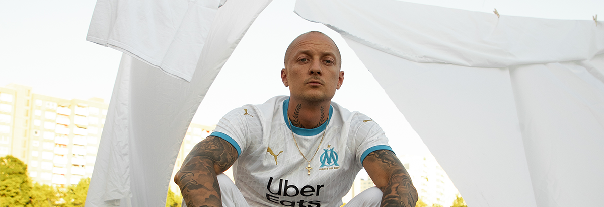 Es ist der Rapper Kurdo zu sehen, der auf einer Dachterasse steht, während im Hintergrund die Sonne untergeht.
